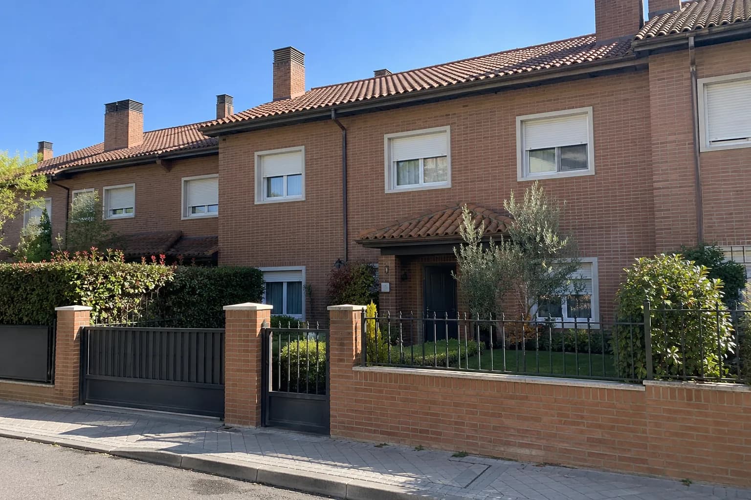 Fachada de un chalet adosado de ladrillo con jardín en las afueras de Madrid